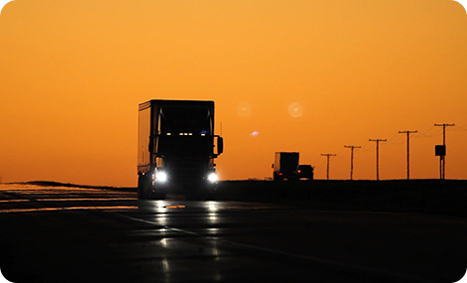 Video still of truck with headlights approaching the camera with telephone poles in silhouette and orange dawn sky